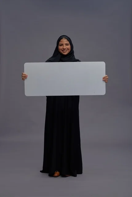 امرأة سعودية بعباءة سوداء تحمل لوحة بيضاء فارغة
