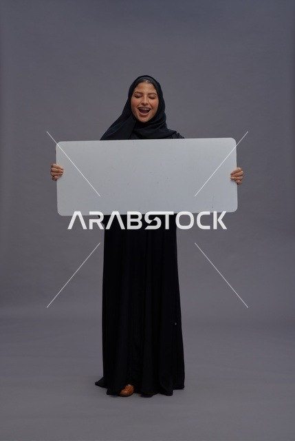 امرأة سعودية بالعباية السوداء تحمل لوحة بيضاء فارغة