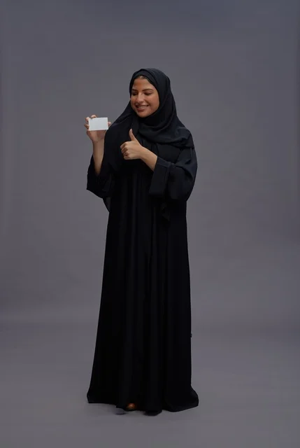 امرأة سعودية بعباية سوداء تحمل بطاقة فارغة وإشارة الإبهام