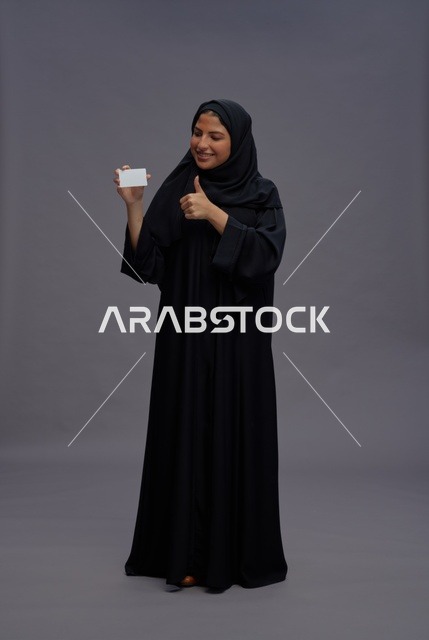 امرأة سعودية بعباية سوداء تحمل بطاقة فارغة وعلامة إعجاب
