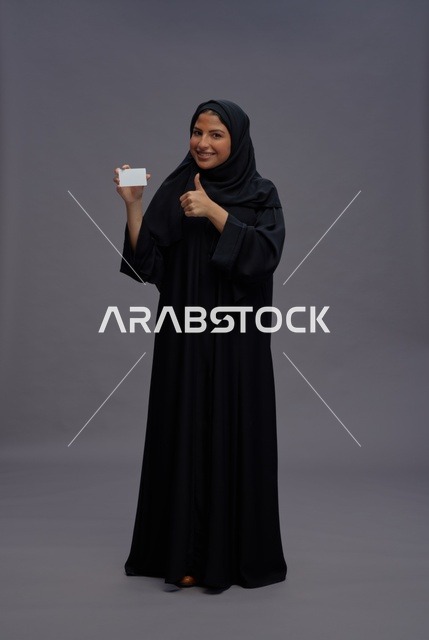 امرأة سعودية بالعباءة تحمل بطاقة فارغة وإيماءة الإعجاب