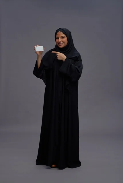 امرأة سعودية بالعباءة تحمل بطاقة فارغة خلفية رمادية