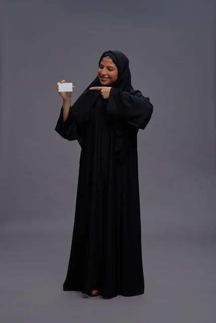 امرأة سعودية بالعباية تمسك بطاقة فارغة في الاستوديو