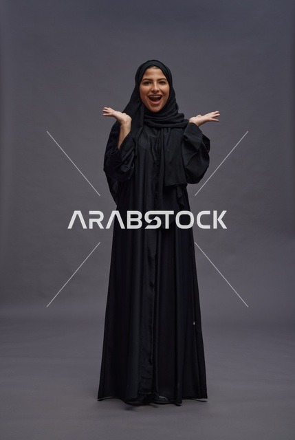 امرأة سعودية مبتهجة بالعباية السوداء بخلفية رمادية