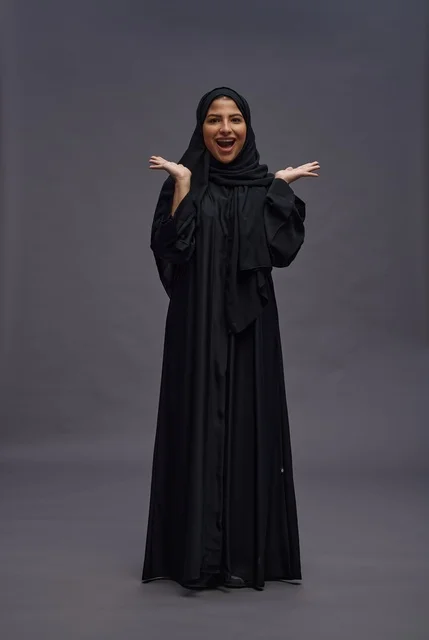 امرأة سعودية مبتهجة بالعباية السوداء بخلفية رمادية