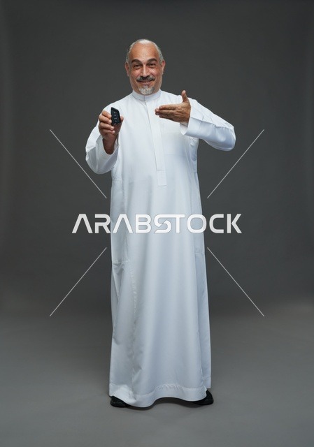 رجل سعودي مسن يحمل مفتاح سيارة في استوديو