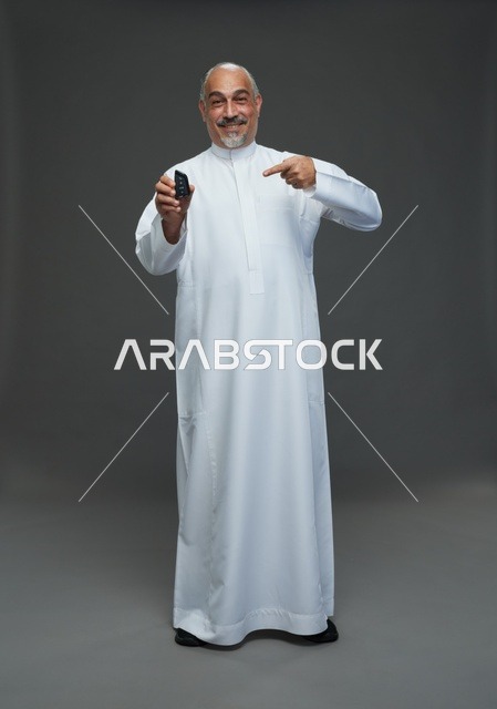 رجل سعودي مسن يبتسم ويحمل مفتاح سيارة بخلفية رمادية