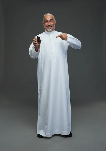 رجل سعودي مسن يبتسم ويحمل مفتاح سيارة بخلفية رمادية