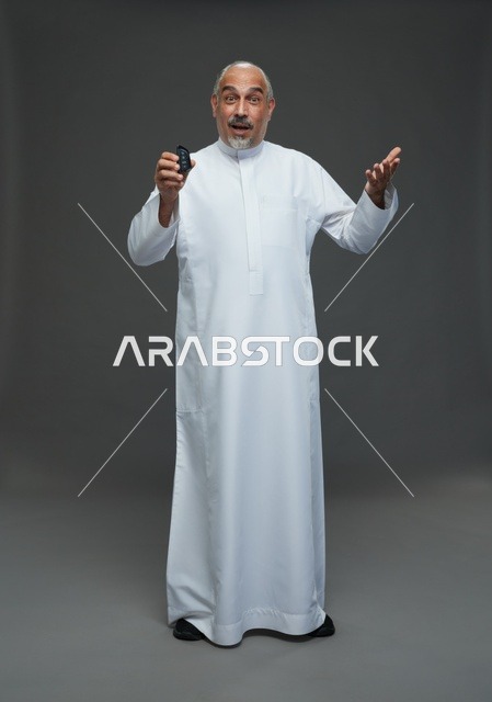 رجل سعودي مسن يرتدي الثوب يحمل مفتاح سيارة بخلفية رمادية