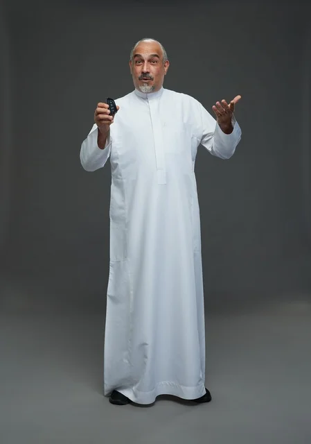 رجل سعودي مسن يحمل مفتاح سيارة بخلفية رمادية