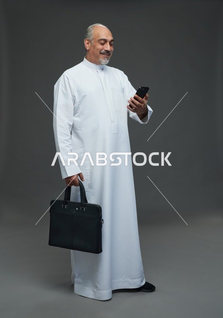 رجل أعمال سعودي مسن يحمل هاتفاً وحقيبة