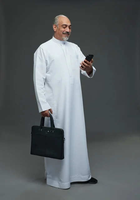 رجل أعمال سعودي مسن يحمل هاتفاً وحقيبة