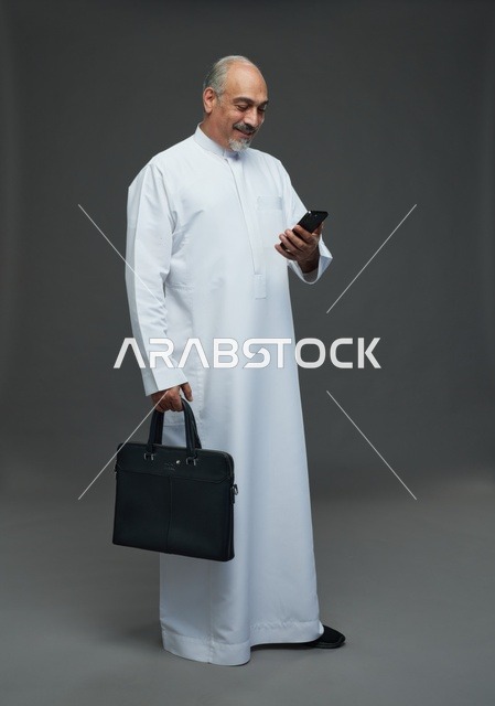رجل أعمال سعودي مسن يحمل هاتفاً ذكياً وحقيبة عمل مهنية