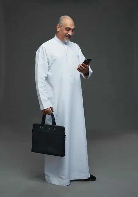 رجل أعمال سعودي مسن يحمل هاتفاً ذكياً وحقيبة عمل مهنية