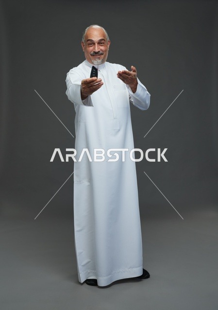 رجل سعودي مسن يحمل مفتاح سيارة بخلفية رمادية