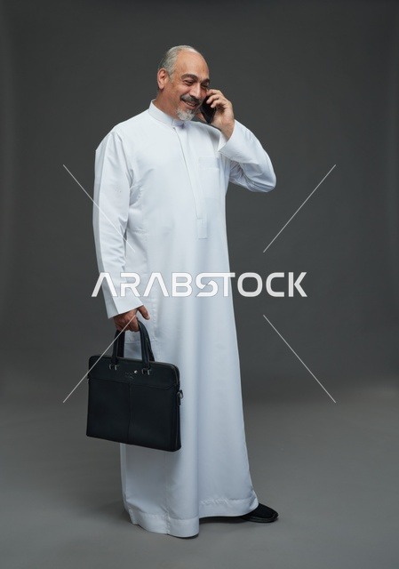 رجل أعمال سعودي بالثوب يتحدث بالهاتف مع حقيبة