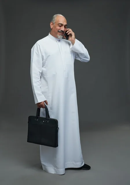 رجل أعمال سعودي مسن يتحدث بالهاتف ويحمل حقيبة أعمال