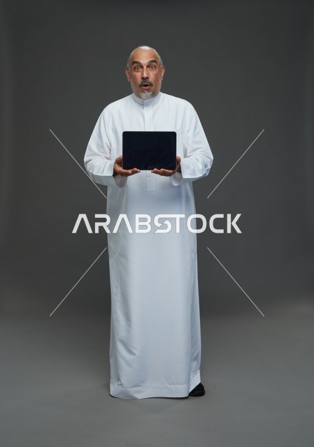 رجل سعودي مسن مندهش يحمل جهاز لوحي رقمي