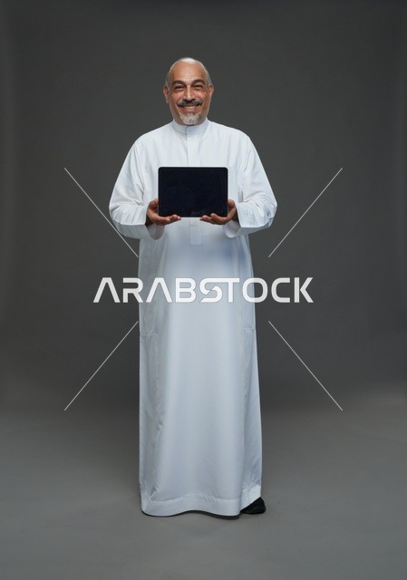 رجل سعودي مسن يحمل جهاز لوحي في الاستوديو