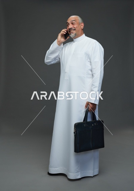 رجل أعمال سعودي مسن يبتسم أثناء مكالمة هاتفية مع حقيبة
