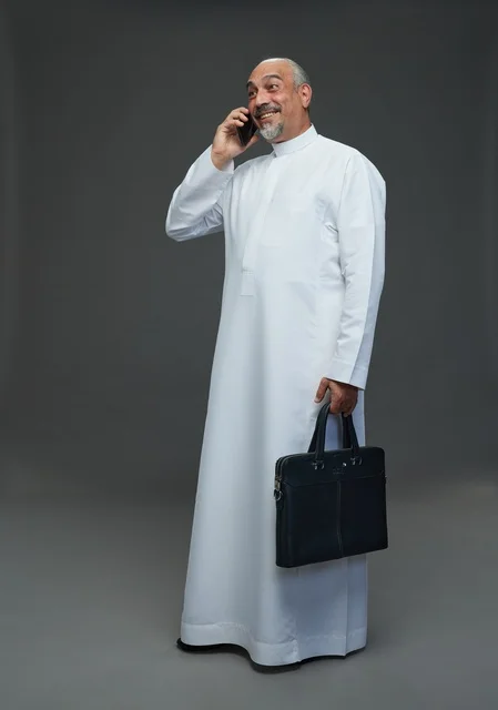 رجل أعمال سعودي مسن يبتسم أثناء مكالمة هاتفية مع حقيبة