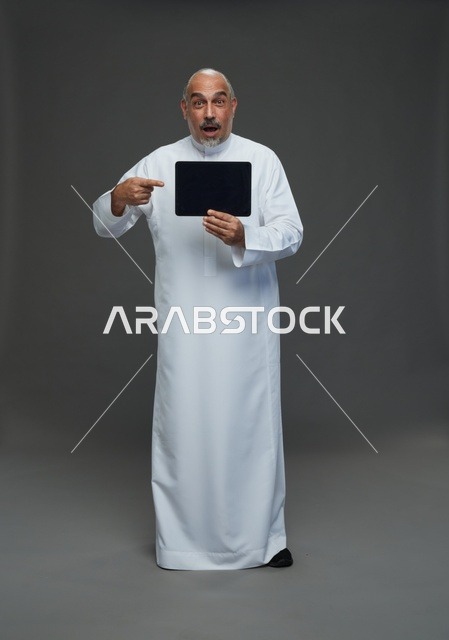 رجل سعودي مسن يحمل جهاز لوحي بتعبير وجه مندهش