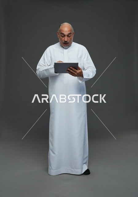 رجل سعودي مسن يستخدم جهاز لوحي بتعبير وجه مندهش للغاية