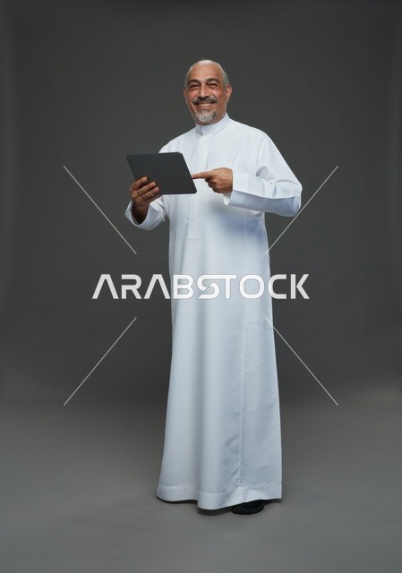 رجل سعودي مسن مع جهاز لوحي بخلفية رمادية