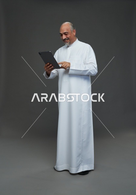 Senior Saudi Man Using Tablet on Gray Background