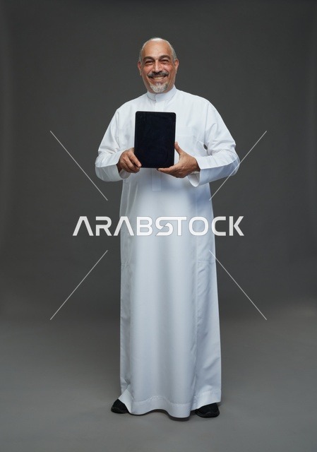 رجل سعودي مسن يحمل جهاز لوحي في الاستوديو