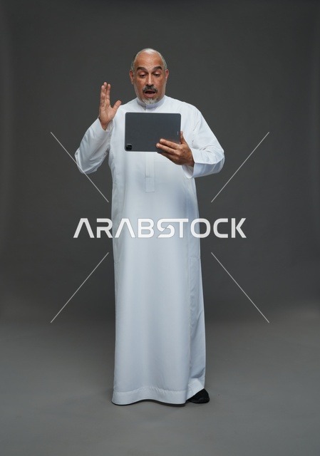 رجل سعودي مسن مندهش يستخدم جهاز لوحي في الاستوديو