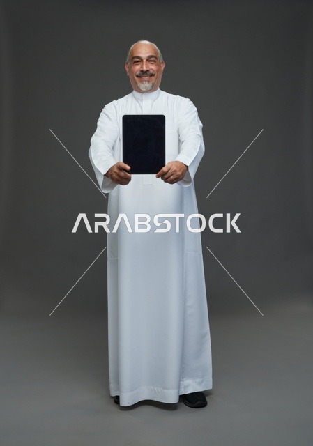 رجل سعودي مسن يحمل جهازاً لوحياً في الاستوديو