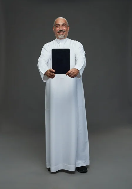 رجل سعودي مسن يحمل جهازاً لوحياً في الاستوديو