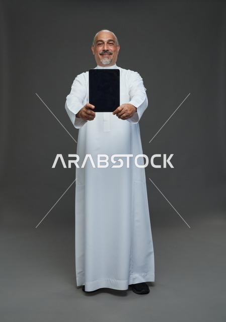 رجل سعودي مسن يمسك بجهاز لوحي في استوديو تصوير