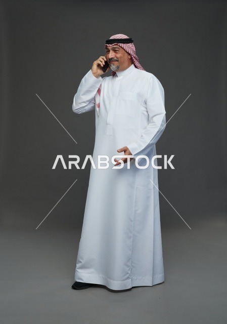 رجل سعودي مسن يتحدث عبر الهاتف المحمول في استوديو رمادي