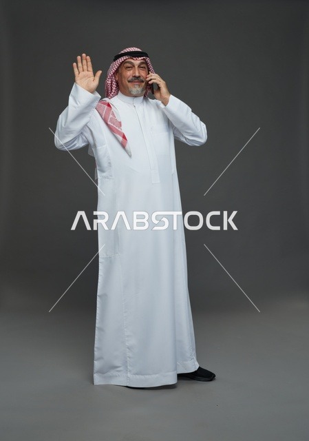 رجل سعودي مسن يتحدث بالهاتف ويرحب بيده