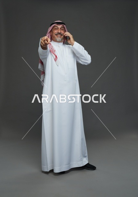 رجل سعودي مسن يتحدث بالهاتف ويشير للكاميرا