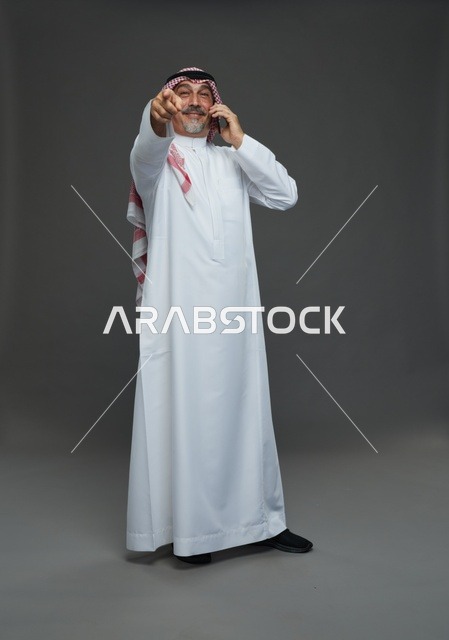 رجل سعودي مسن يتحدث بالهاتف ويشير للأمام