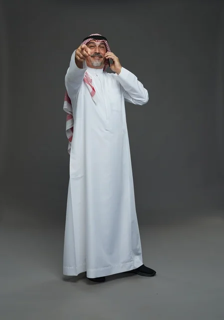 رجل سعودي مسن يتحدث بالهاتف ويشير للأمام