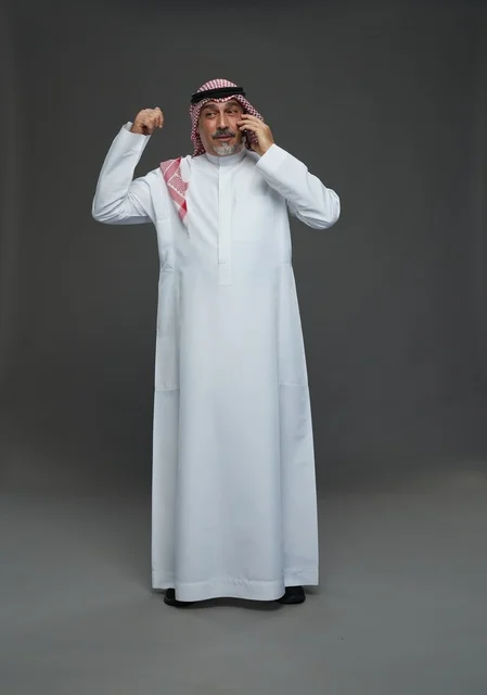 رجل سعودي مسن يحتفل بالنجاح أثناء التحدث في الهاتف المحمول