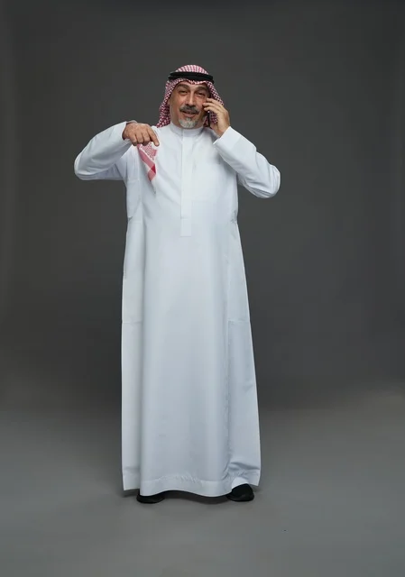 رجل سعودي مسن يتحدث بالهاتف ويشير بإصبعه