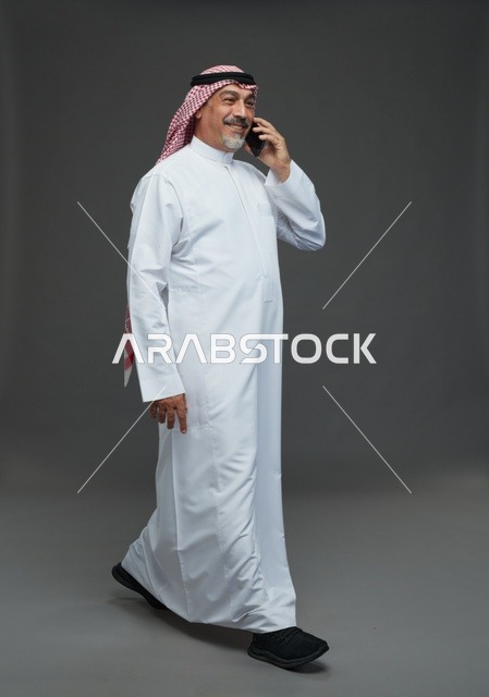 رجل سعودي مسن يتحدث بالهاتف المحمول أمام خلفية رمادية