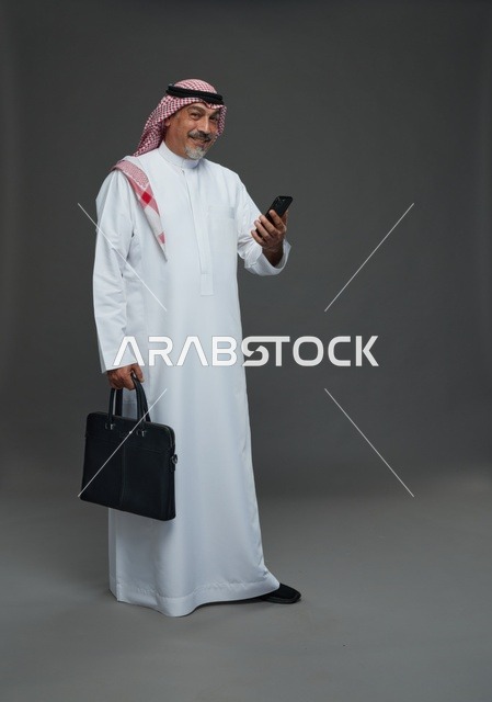 رجل أعمال سعودي مسن يحمل هاتفا ذكيا وحقيبة عمل رسمية