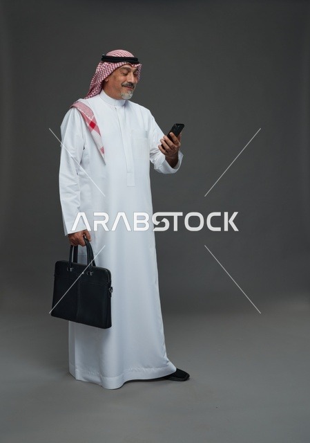 رجل أعمال سعودي مسن يحمل حقيبة وهاتفه المحمول