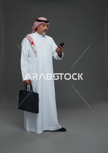 رجل أعمال سعودي مسن يحمل حقيبة ويتفقد هاتفه