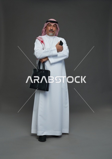 رجل أعمال سعودي مسن يحمل حقيبة عمل وهاتف محمول ذكي