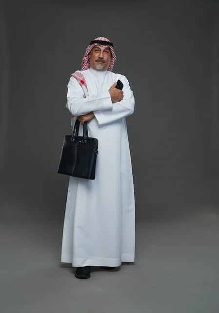 رجل أعمال سعودي مسن يحمل حقيبة عمل وهاتف محمول ذكي