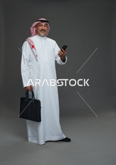 رجل أعمال سعودي مسن يحمل هاتفا وحقيبة عمل