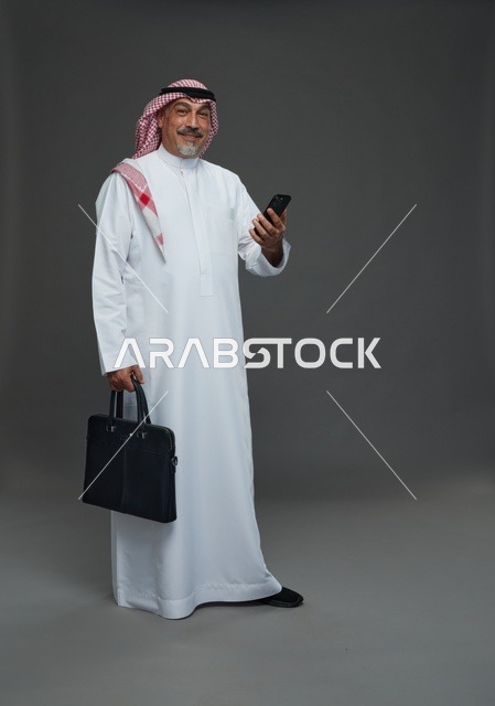 رجل أعمال سعودي مسن يحمل هاتفا وحقيبة عمل