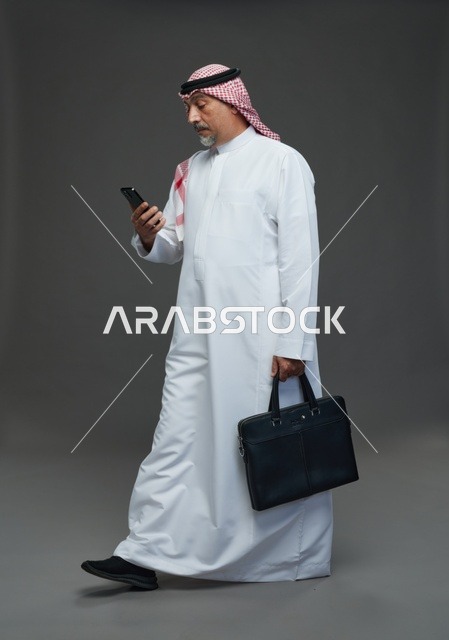 رجل أعمال سعودي مسن يحمل حقيبة وهاتف محمول